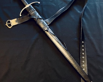 May include: A medieval-style sword with a black leather sheath and belt. The sword features a silver crossguard and pommel, with a black handle. The sheath is intricately detailed with leather wrappings and a gold-colored buckle. The sword is displayed against a dark background.