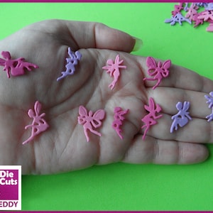 May include: A hand holding a selection of pink and purple fairy cutouts. The cutouts are made from paper and are approximately 1 inch in height. The cutouts are shaped like fairies with wings and flowing dresses. The cutouts are ideal for scrapbooking, card making, and other craft projects.