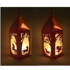 Könnte beinhalten: Zwei rosa Papierlaternen mit ausgeschnittenen Motiven von Einhörnern und Bäumen. Die Laternen sind von innen beleuchtet und strahlen ein warmes Licht aus.