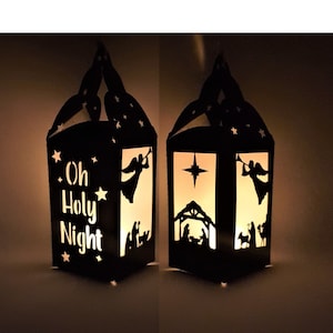 Może przedstawiać: Dwie czarne papierowe lampiony z wyciętymi wzorami. Jeden lampion ma napis "Oh Holy Night" i gwiazdę. Drugi lampion przedstawia scenę narodzin z gwiazdą.