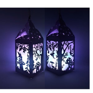 Könnte beinhalten: Zwei schwarze Papierlaternen mit filigranen Ausschnitten, die eine Waldszene darstellen, darunter Bäume, Pilze und ein Reh. Die Laternen werden von innen beleuchtet und erzeugen ein sanftes violettes und blaues Leuchten.
