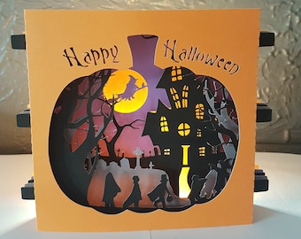 Może przedstawiać: Kartka okolicznościowa na Halloween z wycięciem w kształcie dyni. Wycięcie przedstawia nawiedzony dom, cmentarz, latającą na miotle czarownicę i dzieci chodzące po cukierki. Na kartce widnieje napis "Happy Halloween" czarnymi literami.
