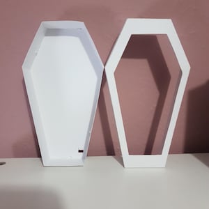 May include: Two white cardboard coffin-shaped boxes, one open and one closed. The boxes are made of sturdy cardboard and have a smooth, white finish.