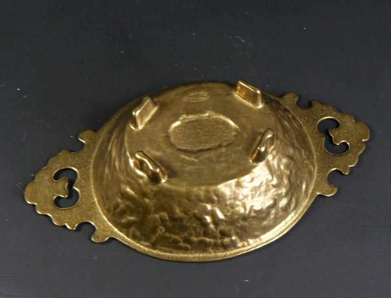 May include: A gold-toned metal serving dish with a hammered finish and ornate handles. The dish has three small feet on the bottom.