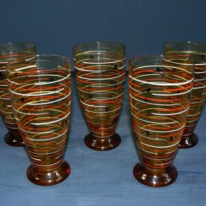 K&ouml;nnte beinhalten: Satz von sechs Trinkgl&auml;sern aus Bernstein-Glas mit einem wirbelnden orange-wei&szlig;en Design und schwarzen Akzenten.