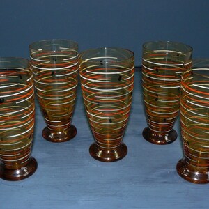 K&ouml;nnte beinhalten: Satz von sechs Trinkgl&auml;sern aus Bernstein-Glas mit einem wei&szlig;en und orangefarbenen Wirbelmuster. Die Gl&auml;ser haben einen klaren Boden und eine abgerundete Form.