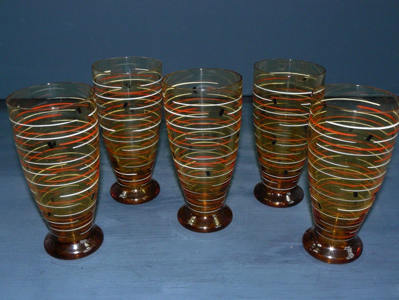 K&ouml;nnte beinhalten: Satz von sechs Trinkgl&auml;sern aus Bernstein-Glas mit einem wei&szlig;en und orangefarbenen Wirbelmuster. Die Gl&auml;ser haben einen klaren Boden und eine abgerundete Form.