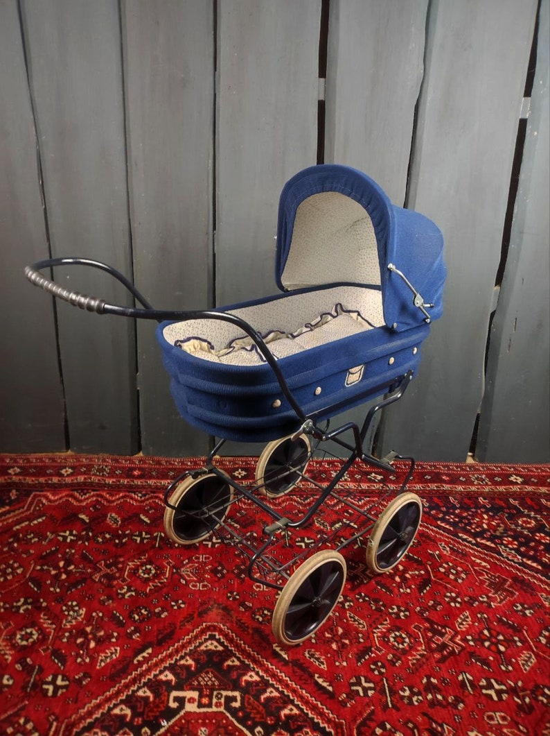 May include: A vintage blue baby stroller with a white and blue patterned lining. The stroller has a black metal frame and four black wheels.