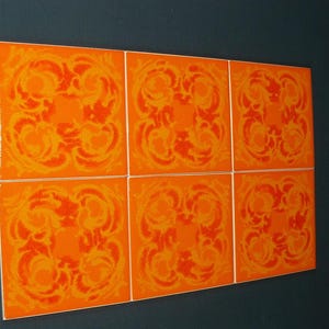 Może przedstawiać: Sześć pomarańczowych płytek ceramicznych z powtarzającym się kwiatowym wzorem w ciemniejszym odcieniu pomarańczu. Płytki ułożone są w siatkę 2x3 i umieszczone na ciemnoniebieskiej ścianie.