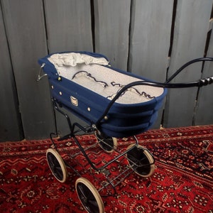 May include: A vintage blue baby stroller with white polka dot lining and black metal frame. The stroller is on a red patterned rug.