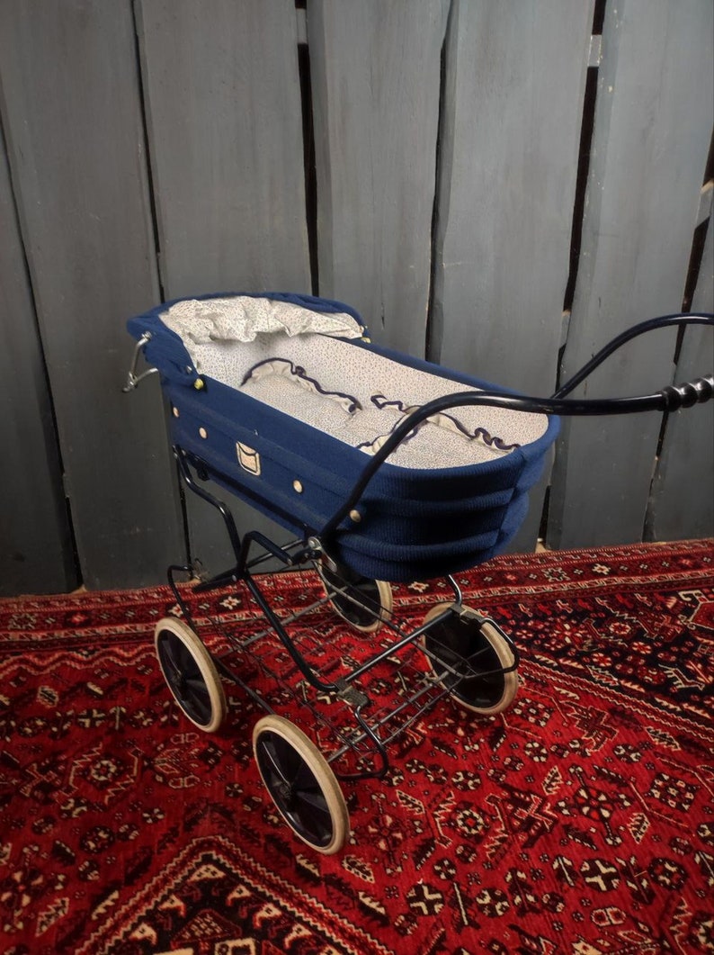 May include: A vintage blue baby stroller with white polka dot lining and black metal frame. The stroller is on a red patterned rug.