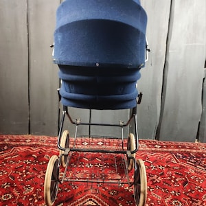 May include: A vintage blue stroller with a black metal frame and a basket underneath. The stroller has three wheels and is on a red patterned rug.