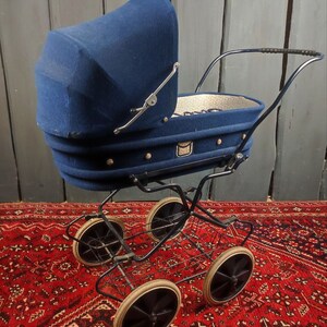 May include: A vintage blue baby stroller with a fabric canopy and a wire basket underneath. The stroller has four wheels and is sitting on a red patterned rug.