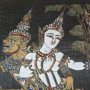 Könnte beinhalten: Ein schwarzes Stoffpanel mit einer handgemalten Szene eines Fabelwesens und einer Frau in traditioneller thailändischer Kleidung. Das Wesen hat ein goldenes Gesicht und einen grünen Körper, während die Frau ein weiß-goldenes Outfit trägt. Die Szene spielt vor einem dunklen Hintergrund mit einem Baum und einem Gebäude im Hintergrund.