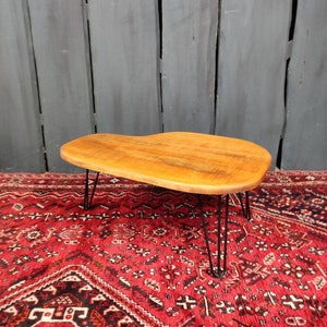 Puede incluir: Una mesa de centro de madera con una forma orgánica única y un acabado de madera natural. La mesa tiene cuatro patas de horquilla negras.