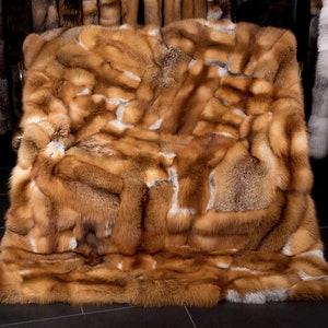 May include: A large, luxurious fox fur throw blanket in shades of orange, brown, and white. The fur is arranged in a patchwork pattern, creating a unique and eye-catching design.