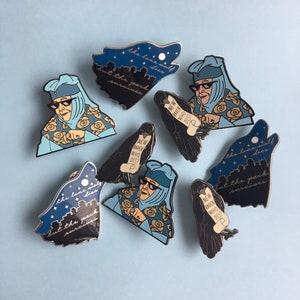 Puede incluir: Colección de pines esmaltados con varios diseños sobre un fondo azul claro. Los pines incluyen una silueta de lobo con texto, un cuervo con un pergamino y un personaje con gafas de sol y un tocado. El texto en los pines dice "the lone wolf dies but the pack survives" y "NEW RAVEN WHO DIS?"