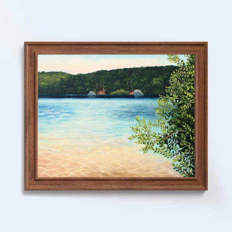 May include: A framed painting depicting a tranquil lake scene. Lush green trees line the shore, with a few boats anchored in the distance. The water is a vibrant blue, reflecting the sunlight. The foreground features a sandy beach and a leafy branch extending from the right side of the frame.