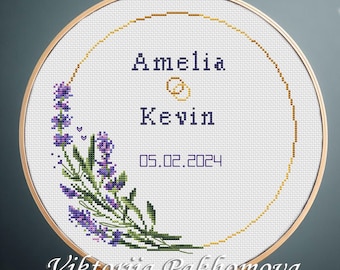 May include: Cross-stitch hoop art featuring the names "Amelia" and "Kevin" with wedding rings and the date 05.02.2024. The design includes a lavender floral arrangement and a gold-colored border. The artist's name, Viktoriia Pakhomova, is at the bottom.