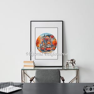 May include: A framed watercolor print depicting a European town scene with a red trolley car. The artwork is in a circular format, framed in black, and features autumn colors. The artist's name, Viktoriia Pakhomova, is printed in cursive.