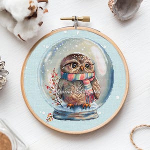 Schema punto croce gufo con sfera di neve in formato PDF. Simpatico e divertente uccello invernale con sfera di vetro pittorica ricamata. Disegno natalizio, decorazione per la cameretta dei bambini.