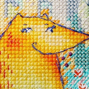 Op de afbeelding: Een close-up van een gele vos met blauwe ogen en een glimlach, geborduurd op een witte stof met een kleurrijk bloemenpatroon.