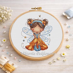 May include: A cross-stitch embroidery of a fairy in a wooden hoop. The fairy has brown hair, a blue headband, and orange and blue wings. She wears an orange dress and blue boots. The text "Viktoriia Pakhomova" is on the hoop.