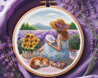May include: Cross-stitch embroidery in a wooden hoop depicts a woman in a straw hat in a lavender field. A basket of sunflowers, a sleeping cat, and a teacup are also shown. The artist's name, Viktoria Pakhomova, is at the bottom.