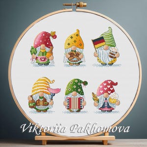 May include: Six colorful gnomes with different accessories, including a pretzel, a flag, a beer stein, a sausage, an accordion, and a flower. The gnomes are embroidered on a white background.