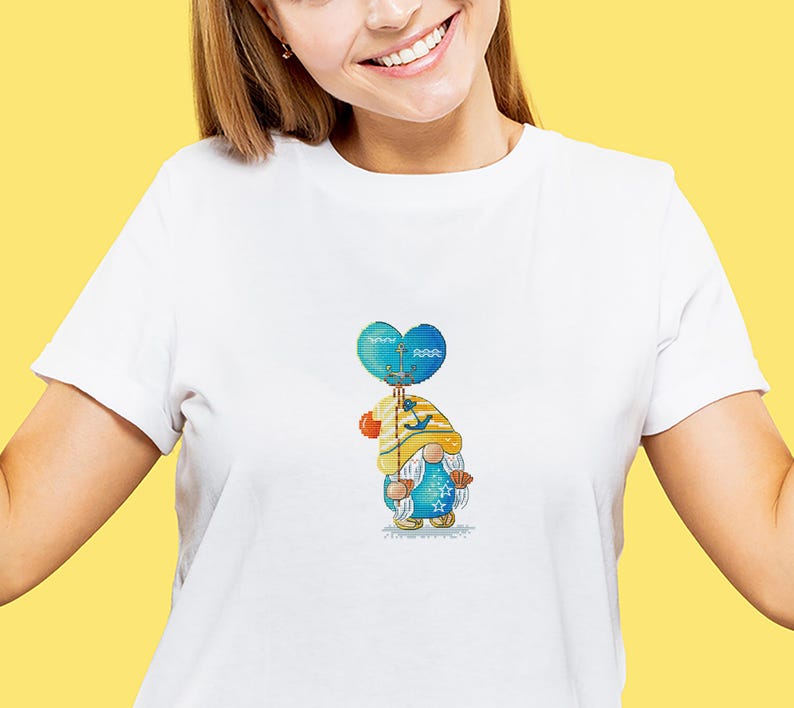 May include: White t-shirt featuring a colorful gnome design. The gnome is holding a blue heart-shaped balloon with a nautical theme. The gnome wears a yellow hat and blue outfit with star and seashell details.