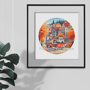 May include: Framed cross-stitch artwork featuring a circular design of a European town with a red tram. The scene includes colorful buildings, trees with orange leaves, and the text "Viktoriia Pakhomova". The artwork is set against a light gray background.