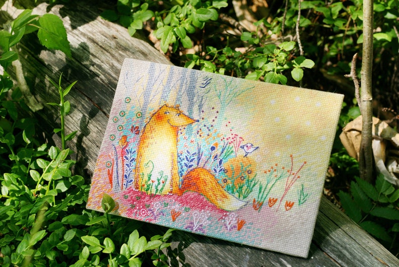 Op de afbeelding: Een borduurwerk met kruissteek, waarop een vos in een bos zit met een klein vogeltje dat op een tak zit. De vos is oranje en wit, en de achtergrond is een kleurrijke mix van groen, blauw en geel.