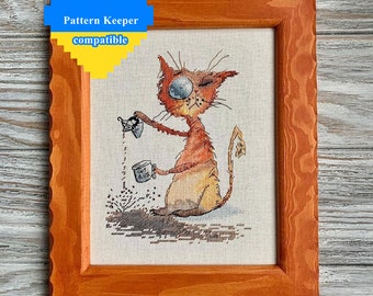 May include: Cross-stitch art of a cartoon cat pouring from a small cup, framed in a rustic, orange-toned wooden frame. The cat is orange and yellow, with a large, expressive eye. The text "Pattern Keeper compatible" is in the upper left corner.