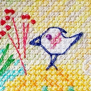 Op de afbeelding: Geborduurde vogel met blauwe vleugels en een wit lichaam, gepercht op een gele achtergrond met roze en rode bloemen.