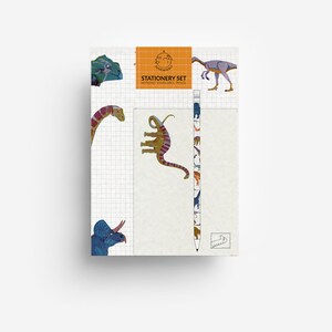 Könnte beinhalten: Ein Schreibwarenset mit einem karierten Notizblock, der mit verschiedenen Dinosaurier-Illustrationen wie einem Triceratops verziert ist. Das Set enthält einen Stift mit Dinosaurier-Aufdruck und ein orangefarbenes Etikett mit der Aufschrift STATIONERY SET.