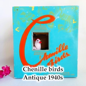 Może przedstawiać: Winietkowe pudełko na ptaki z chenille, z niebieskim tłem, dużą pomarańczową literą 'C' i napisem 'Chenille Birds' w kolorze pomarańczowym. Pudełko ma małe okienko, które pokazuje białego ptaka z chenille w budce dla ptaków. Na spodzie pudełka znajduje się napis 'Chenille birds Antique 1940s'.