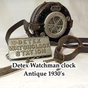 May include: Antique Detex Watchman clock dating from the 1930s. The clock is black with a silver face and a leather strap. The clock has a metal tag that reads "Detex Watchclock Station".