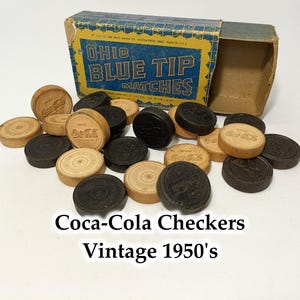 Peut inclure: Jeu de dames Coca-Cola vintage des années 1950. L'ensemble comprend des dames en bois noir et marron clair, certaines avec le logo Coca-Cola. Les dames sont éparpillées autour d'une boîte d'allumettes Ohio Blue Tip ouverte.