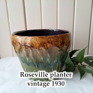 Op de afbeelding: Een bruine en groene geglazuurde keramische plantenpot met een vintage ontwerp uit de jaren 1930.  Roseville planter vintage 1930.