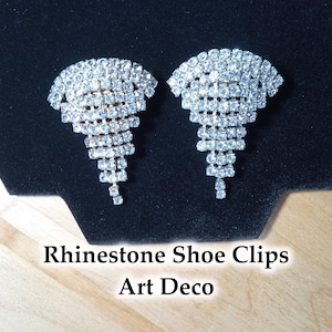 May include: Two Art Deco rhinestone shoe clips. Each clip features a cascading design of clear, sparkling rhinestones. The clips are displayed on a black surface with the text "Rhinestone Shoe Clips Art Deco".