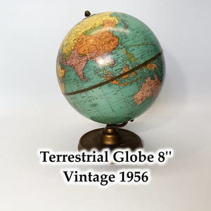 May include: Vintage 1956 terrestrial globe, 8 inches in diameter, with a teal and tan color scheme. The globe is mounted on a brass-colored base. The text "Terrestrial Globe 8" Vintage 1956" is displayed below the globe.