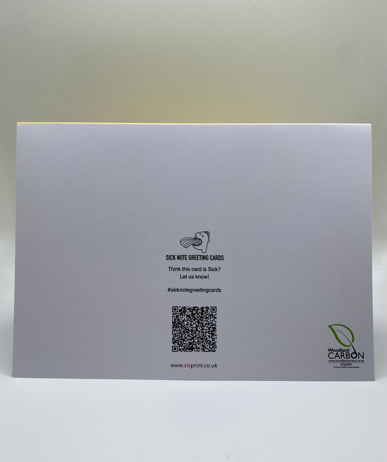 May include: A white greeting card with a black and white illustration of a person with a speech bubble saying "Sick Note Greeting Cards". The card has a black and white QR code and the text "Think this card is Sick? Let us know! #sicknotegreetingcards www.sixprint.co.uk" printed on it. The card also has a black and white logo for Woodland Carbon.