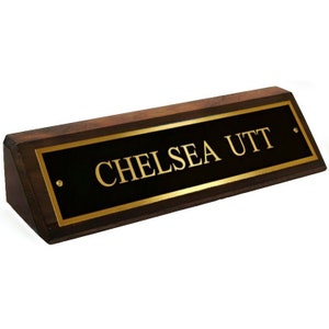 May include: A dark brown wooden desk nameplate with a gold plaque that reads "CHELSEA UTT".