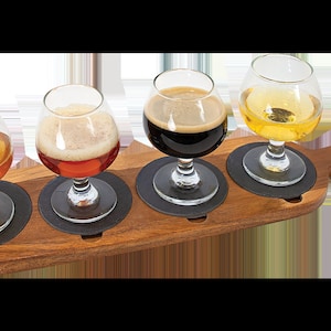 May include: A wooden beer flight paddle with four glasses, each holding a different type of beer. The beers range in color from light amber to dark brown. Each glass sits on a black coaster.
