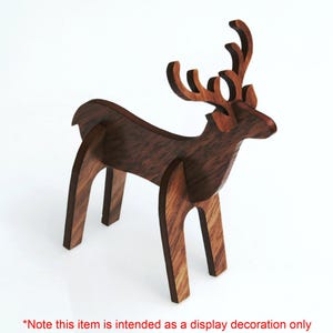 May include: A wooden reindeer figurine with a brown wood grain finish. The reindeer has a stylized design with simple, geometric shapes. The reindeer is standing on a white surface.