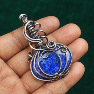 May include: A blue lapis lazuli gemstone pendant wrapped in copper wire. The wire is twisted and curled into an intricate design.