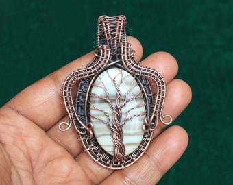 May include: A copper wire wrapped pendant featuring a white and brown agate stone with a tree design. The pendant is oval shaped and has a loop at the top for attaching to a chain.
