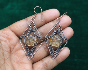 May include: A pair of earrings with a geometric design featuring a yellow carved flower in the center of each earring.