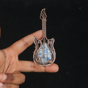 May include: A copper wire wrapped guitar pendant with a blue and gray stone inlay.