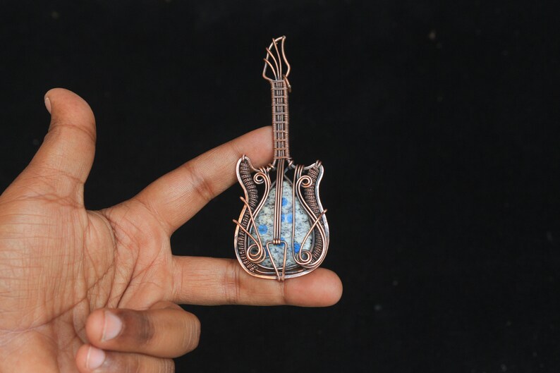 May include: A copper wire wrapped guitar pendant with a blue and gray stone inlay.
